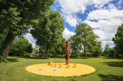 Ein Park mit einem gelben Kreis und einem hohen, zylindrischen Objekt in der Mitte, umgeben von Bäumen und Gras. (KI generiert)