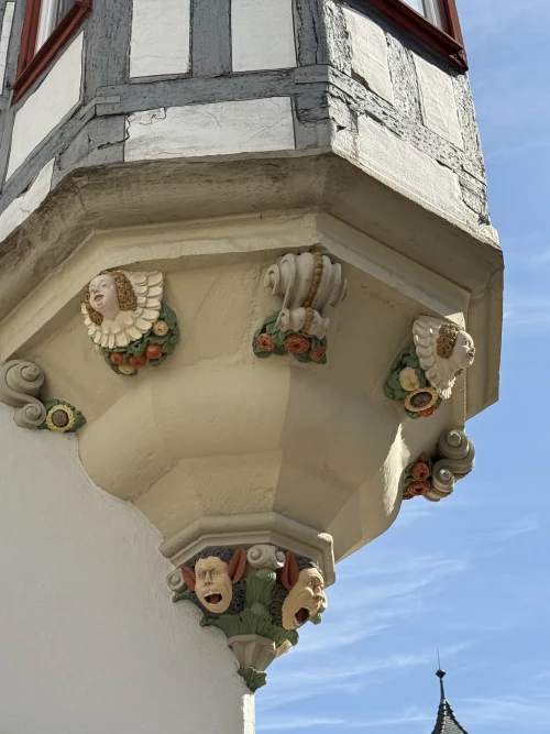 Ein Gebäude mit verzierten Gesichtern und Blumen an der Ecke. (KI generiert)