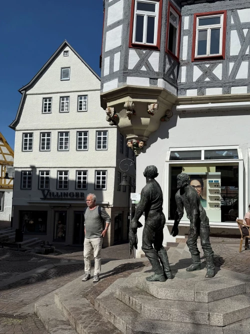 Historisches Fachwerkhaus mit zwei Personen vor einem Brunnen in Altstadtgasse. (KI generiert)