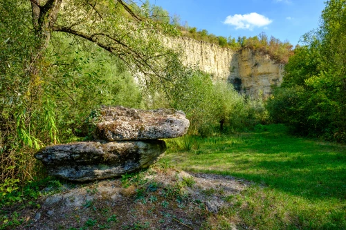 Ein großer Stein in einer grünen Landschaft vor einem Felsen. (KI generiert)
