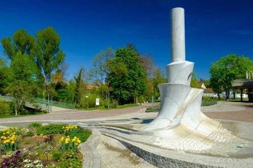Moderne Skulptur aus Metall mit Wasserbecken und Blumenbeet im Park. (KI generiert)