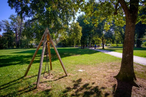 Ein Holzgestell mit Seilen in einem Park mit Bäumen und Wegen. (KI generiert)