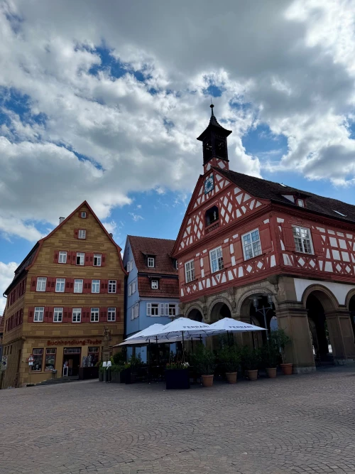 Historische Gebäude mit Fachwerk und Schildern, davor ein Café mit Sonnenschirmen und Tischen. (KI generiert)