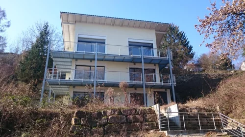 Modernes Haus mit zwei Balkonen auf einem Hügel, umgeben von Natur. (KI generiert)