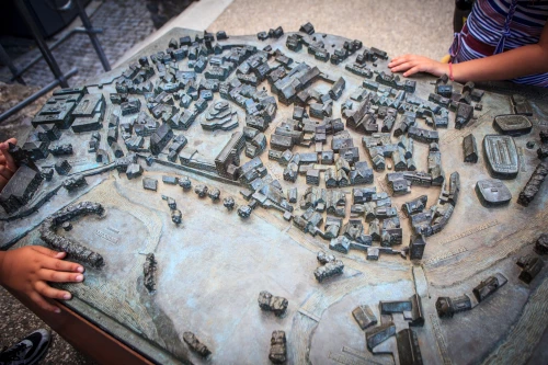 Modell einer Stadt mit vielen Gebäuden und Straßen, zwei Personen berühren das Modell. (KI generiert)