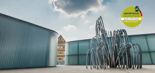 Moderne Metallskulptur vor Industriegebäuden, Wanderzeichen im Himmel. (KI generiert)