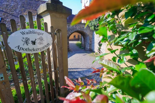 Holztor mit ovalem Schild "Waiblinger Apothekergarten" und Steinbogen im Hintergrund. (KI generiert)