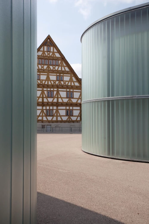 Ein Fachwerkhaus mit einem modernen Gebäude im Vordergrund. (KI generiert)