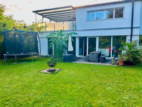 Ein Garten mit Trampolin und Haus im Hintergrund. (KI generiert)