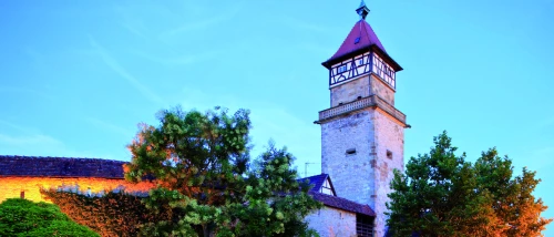 Ein beleuchteter Turm mit einem spitzen Dach und Fachwerk im Abendhimmel. (KI generiert)