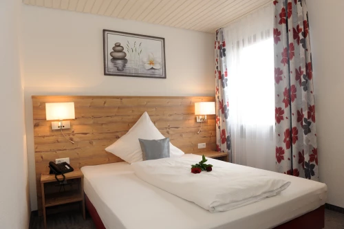 Ein gemütliches Hotelzimmer mit einem Doppelbett und Blumen auf der Bettdecke. (KI generiert)