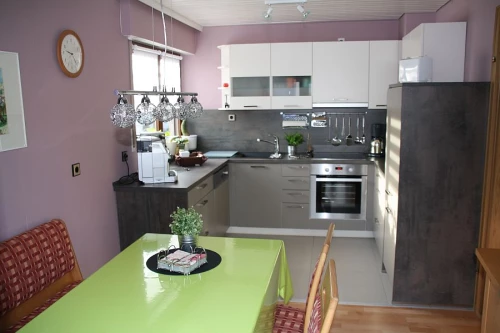 Moderne Küche mit grünem Esstisch und lila Wänden (KI generiert)