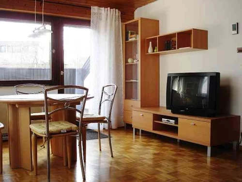 Wohnzimmer mit Esstisch, Stühlen, TV und Regalen. Große Fenster mit Vorhängen. (KI generiert)