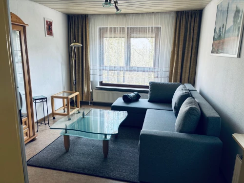 Ein gemütliches Wohnzimmer mit Sofa, Glastisch und großen Fenstern. (KI generiert)