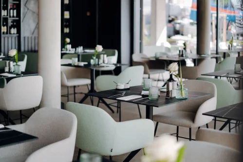 Ein modernes Restaurant mit grünen Stühlen und schwarzen Tischen, durch große Fenster hell beleuchtet. (KI generiert)