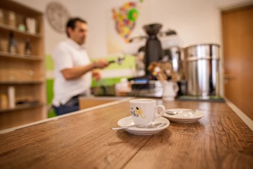 Eine Tasse Kaffee auf einem Tablett mit einem Löffel. Im Hintergrund ein Mann, der etwas hält. (KI generiert)