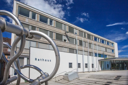 Moderne Rathausfassade mit Metallskulptur im Vordergrund, klarer Himmel. (KI generiert)