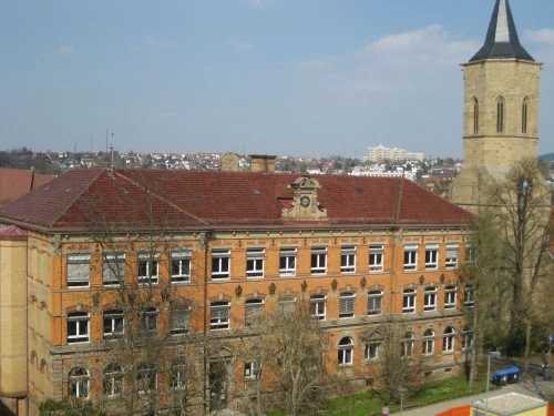 Großes rotes Backsteingebäude mit Uhrturm und Stadt im Hintergrund. (KI generiert)