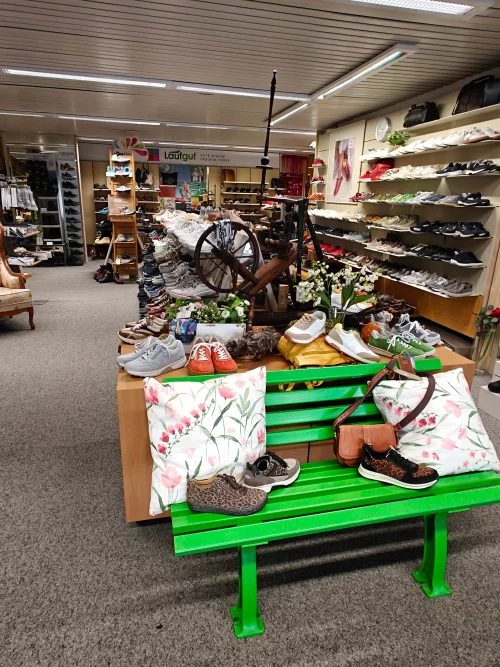 Schuhgeschäft mit verschiedenen Schuhen und Accessoires auf einer grünen Bank und Regalen. (KI generiert)