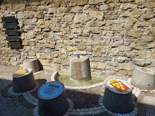 Steinmauer mit Graffiti und drei Farbdosen (blau, gelb, rot) auf dem Boden. (KI generiert)