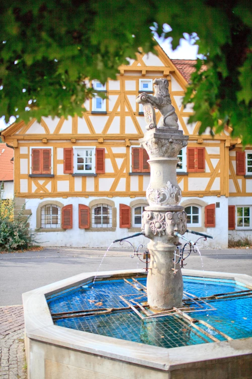 Barocke Brunnenfigur mit Putten auf Sockel vor Fachwerkhaus in Waiblingen. (KI generiert)