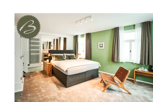 Ein Schlafzimmer mit einem großen Bett, einem Stuhl und einem Schreibtisch. Die Wände sind grün gestrichen und es gibt Vorhänge an den Fenstern. (KI generiert)