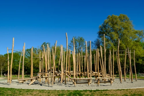 Holzspielplatz mit verschiedenen Klettergerüsten und Bäumen im Hintergrund (KI generiert)