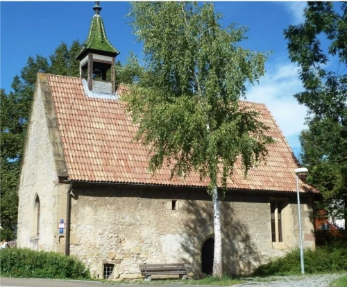 Alte Kirche mit Steinen und rotem Dach, umgeben von Bäumen. (KI generiert)