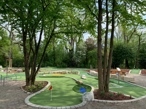 Ein Minigolfplatz mit grünen Bahnen und Hindernissen in einem Park. (KI generiert)