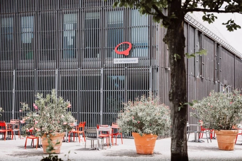 Außenbereich eines Cafés mit roten Stühlen und Pflanzen in Töpfen. (KI generiert)