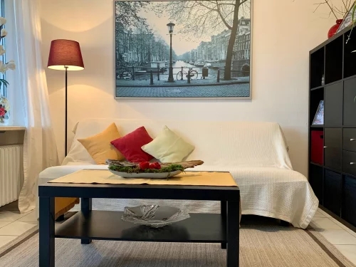 Ein gemütliches Wohnzimmer mit Sofa, Kissen und einem Blumenarrangement auf dem Tisch. (KI generiert)