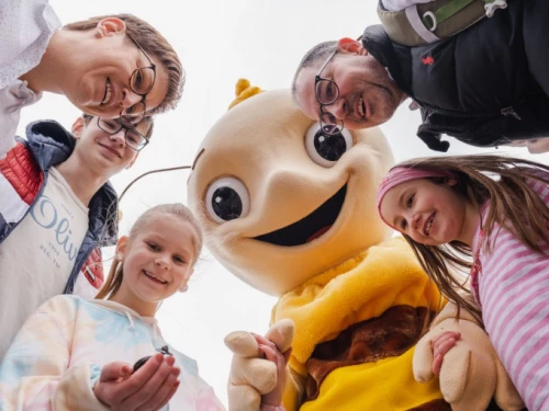 Eine Familie mit einem gelben Maskottchen, alle lächeln in die Kamera. (KI generiert)